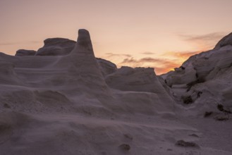 Dramatic sunset casting a warm glow over the sculptural white rock formations of Sarakiniko on the