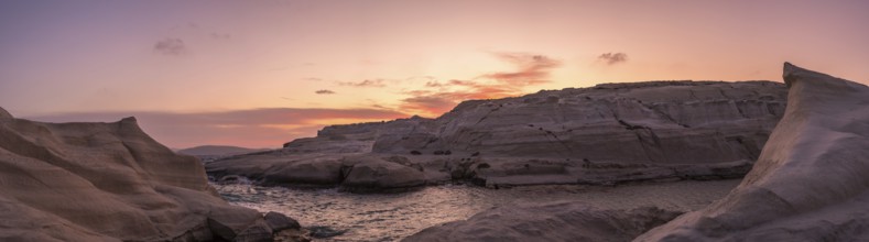 Sweeping panoramic view of Sarakiniko beach on Milos Island, Greece, under a vibrant sunset sky.