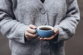 A person in a cozy gray sweater holds a blue cup coffee, capturing a peaceful moment of warmth and