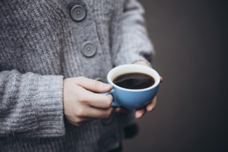 A person in a cozy sweater holds a steaming cup of coffee, providing warmth and comfort on a chilly
