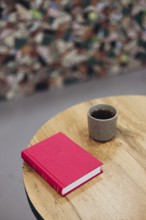 A serene setting featuring a red book and a cup of coffee on a wooden table of a bookstore, ideal