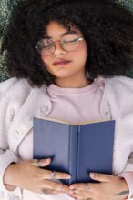 A peaceful latin woman in glasses rests with a book on a cozy day indoors. The scene captures