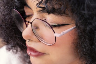 A detailed close-up shot of a latin woman wearing glasses. The focus highlights their piercings,