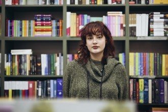 A young woman stands confidently in front of a vibrant, well-stocked bookcase, her expression