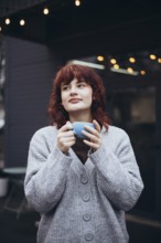 A young woman enjoys a coffee in a cafe terrace, wearing a cozy sweater, surrounded by string
