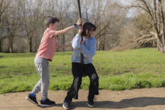 Two friends enjoy a sunny day at the park, playing on a zip line with grassy scenery. The joy of