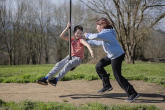 Two friends enjoy a sunny day by playing on a zip line in a park. Laughter and joy fill the air as