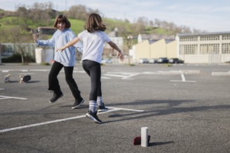 Two friends joyfully dance and play an outdoor game in an empty urban parking lot. Skateboards rest