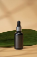 A sleek cosmetic bottle with a dropper cap sits elegantly on a soft beige background. A green leaf