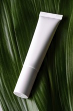 A minimalist presentation of a white cosmetic tube elegantly placed on vibrant green leaves,