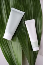 Two white cosmetic tubes lay elegantly on a large, vibrant green leaf, symbolizing natural and