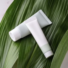 Two unbranded cosmetic tubes rest on a vibrant green tropical leaf, symbolizing eco-friendly and