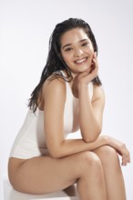 A young female model with a radiant smile and wet hair posing in a studio setting, dressed in a