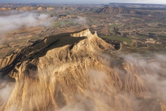 A breathtaking aerial view of rugged mountains partially covered in mist, surrounded by patchwork