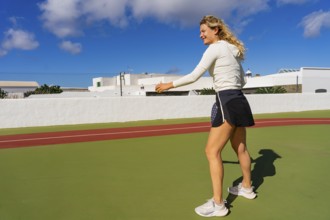 A young woman with curly blonde hair is actively playing tennis, captured in a side profile as she