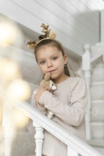 A young girl, dressed in a soft beige sweater adorned with pearls, celebrates Christmas. She wears