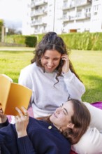A young women smiles while lying down looking at her partner, who is reading from an orange book in