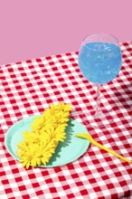 A vibrant summer picnic scene featuring a glass of iced blue beverage and a plate with yellow