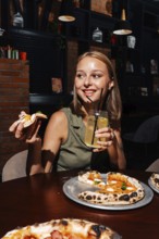 A cheerful person enjoys a slice of Margherita pizza paired with a glass of refreshing citrus