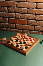 A checkers board on a green surface features chicken nuggets as game pieces. Set against a rustic