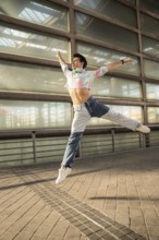 A young man in a colorful shirt and jeans joyfully leaps against a modern urban backdrop. He wears