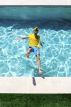 A joyful person in a colorful outfit splashes into a clear blue pool on a sunny day, expressing fun