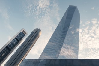 A low-angle view of modern skyscrapers against a cloud-dotted sky in an urban setting. The image