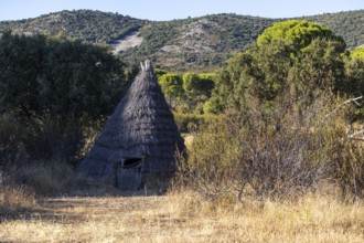 Traditional straw-roofed cabin nestled in the dry grasslands of Cabaneros National Park at sunset,