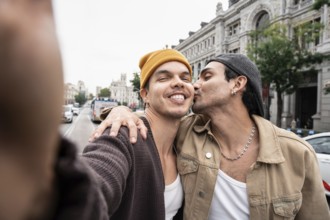 A joyful Colombian gay couple expresses affection on a bustling city street. Captured in a candid
