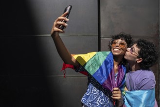 A joyful multiethnic LGBTQ+ couple takes a selfie wrapped in a rainbow flag, symbolizing pride and