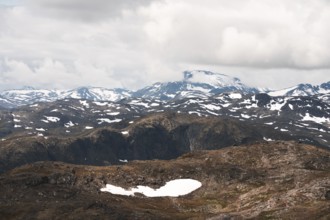 A stunning view of Norway's rugged mountains, dotted with patches of snow The dramatic clouds and