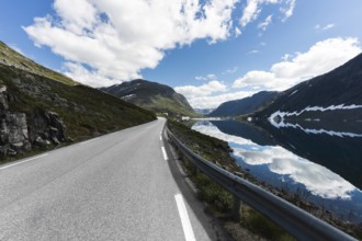 A stunning road in Norway stretches into the distance, flanked by majestic mountains and a