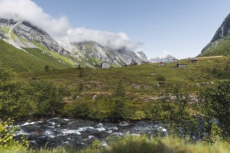 A serene mountain village nestled in a lush green valley in Norway, surrounded by towering peaks