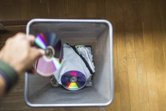 A hand discards CDs into a trash bin, symbolizing the shift from physical media to digital formats.