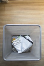A top down view of a trash bin containing used pill packaging and other waste, set on a wooden