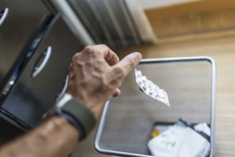 A hand disposes of an blister pack into a mesh waste bin. The casual scene highlights medication