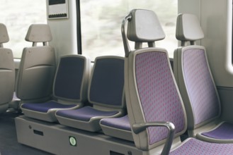 A row of empty train seats with purple upholstery and patterned design by a window. The setting