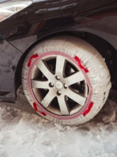 A close-up of a car's wheel equipped with a red snow chain, partially covered in snow, highlighting