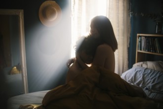 A couple sits on a cozy bed, enveloped in a peaceful embrace. Soft morning sunlight streams through