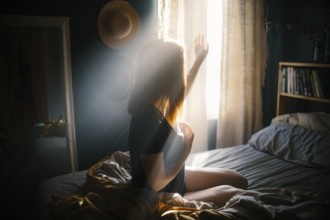 A woman sits on a bed, bathed in morning sunlight streaming through the window. The warm glow