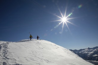 Two skiers hike up a snow-covered mountain under a bright sun, ready for an exhilarating freeride