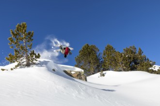A snowboarder performs a backflip against a clear blue sky in a snow covered mountain landscape.
