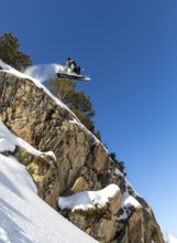 A snowboarder performs an impressive jump off a snow covered cliff, showcasing athleticism and