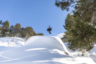 A snowboarder soars through the clear blue sky, performing an aerial trick above a snowy mountain