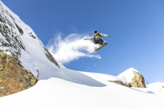 A snowboarder executes an impressive jump, sending a spray of snow flying. The scene is set against