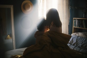 A couple shares an intimate embrace on a bed, bathed in warm morning light streaming through a