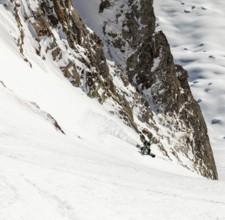 A snowboarder skillfully descends a steep, snowy slope surrounded by rugged cliffs and untouched