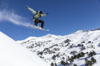Snowboarder performs a jump on snowy mountain slope, surrounded by a breathtaking winter landscape.