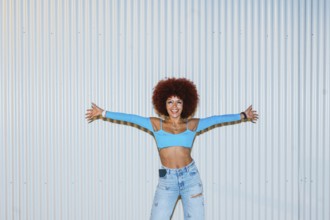 African descendent woman with vibrant afro hair, wearing a bright blue top and jeans, poses