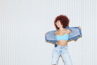A joyful African descent woman with voluminous afro hair wearing light blue denim jeans, a crop